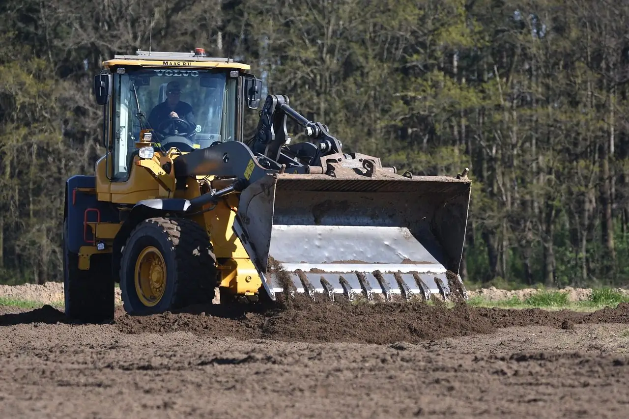 Loader working on a muddy site beside a line of trees